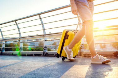 Gezgin adam sarı bavulla şehirde yürüyor.