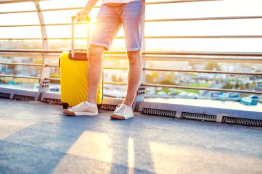 Gezgin adam sarı bavulla şehirde yürüyor.