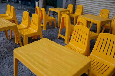 Bright yellow plastic tables and chairs arranged outdoors on a stone pavement. clipart