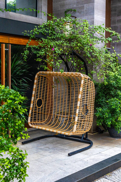 Современный ротанг висит стул в открытом патио настройки с зеленью.