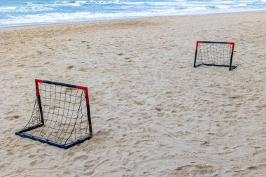 Okyanus dalgalarının yakınındaki kumlu sahilde küçük hedefleri olan plaj futbolu takımı..
