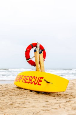 Güvenlik için kırmızı can simidi olan kumlu sahilde parlak sarı sörf kurtarma tahtası..