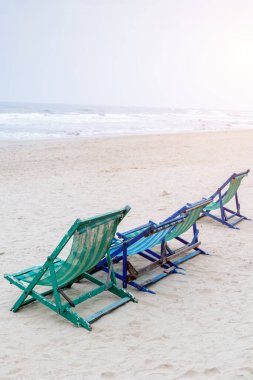 Kumlu sahilde boş plaj sandalyeleri. Gün batımında sakin okyanus dalgaları..