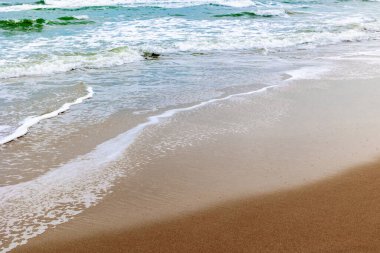 Kumlu sahilde sakin dalgalar, yumuşak dalgalar ve açık gökyüzü..