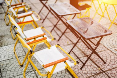 Güneşli verandada katlanabilir sandalye ve masalarla açık hava oturma düzeni.