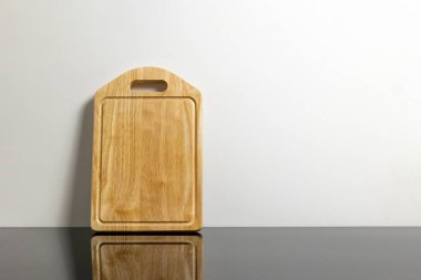 Yansıtıcı siyah yüzey üzerinde tahta kesme tahtası beyaz duvara karşı.