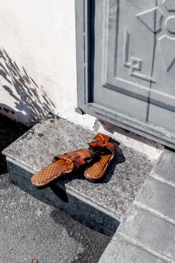 Kahverengi deri sandaletler taşın üzerinde. Gri kapının yanında, açık havada..