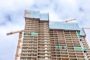 Gökdelen inşaatı, bulutlu bir gökyüzüne karşı vinçler ve cam cephe.