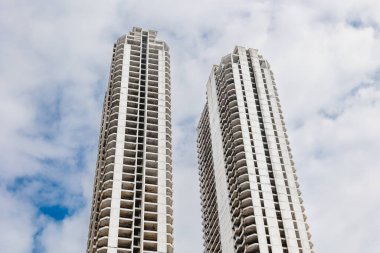 Bulutlu bir gökyüzüne karşı bitmemiş iki uzun gökdelen manzarası.