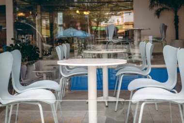 Beyaz sandalyeleri ve cam duvarları olan modern açık hava kafesi..