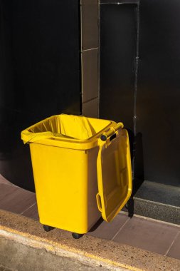 Açık kapaklı parlak sarı çöp tenekesi.