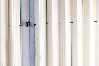 Dikey panelleri ve paslı menteşeleri olan beyaz metal katlanabilir garaj kapısı..