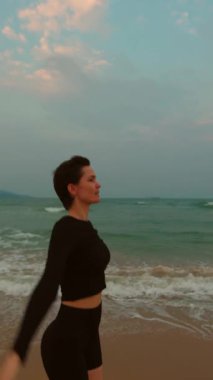 Okyanus dinamiğiyle egzersiz yapan bir kadın günbatımı plaj atmosferinde geriliyor.