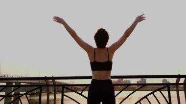 Şehir ortamında gün doğumunda nehir kenarında yoga yapan bir kadın.