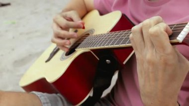 Sahilde akor ilerlemeleri ve parmak hareketlerinin yakın çekimleriyle akustik gitar tıngırdatmak