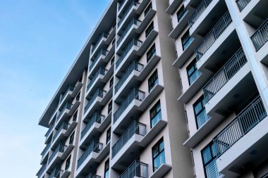Açık mavi gökyüzüne karşı birden fazla balkonu olan modern, yüksek katlı bir apartman..