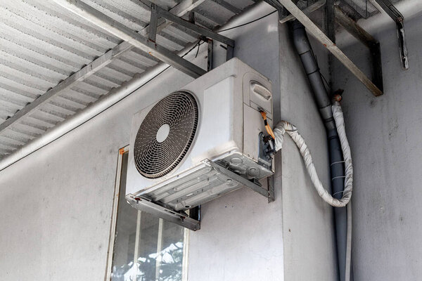 Наружный кондиционер, установленный на белой стене с металлической опорой.