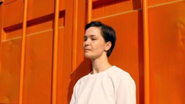 Kalın turuncu duvara yaslanan kişi, şehir ortamında yalnızlığı ve farkındalığı vurguluyor.