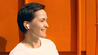 Neşeli kadın açık havada canlı turuncu duvarın karşısında müzikten hoşlanıyor.