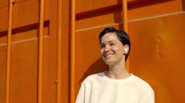 Parlak turuncu arka planlı canlı şehir ortamında müzik dinleyen neşeli kişi