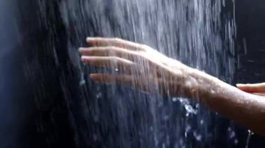 Yumuşak aydınlatma ve sakin atmosfer içinde yavaşça düşen suyla etkileşen yumuşak eller.