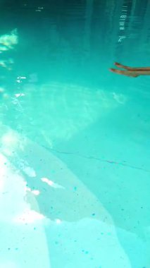 Sakin el hareketi, berrak mavi havuz suyunda dalgalanmalar yaratır.