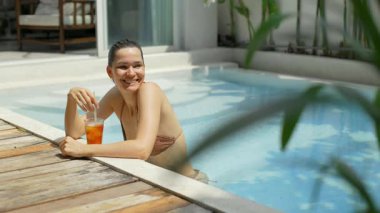 Rahat bir kadın güneşli bir günde havuz kenarında serinletici içkinin tadını çıkarıyor.