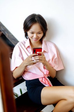 Genç Asyalı kadın, gündelik ortamında akıllı telefon kullanıyor..