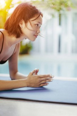 Güneş ışığında havuz kenarında yoga yapan Asyalı genç bir kadın..