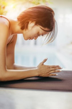 Asyalı genç bir kadın gün doğumunda havuz kenarında yoga yapıyor..