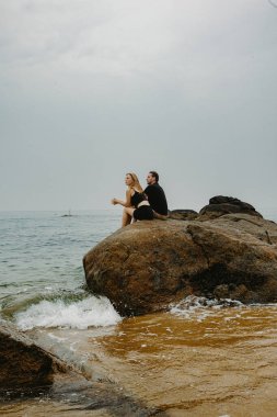 Kafkasyalı çift bulutlu bir günde okyanusun kıyısında kayalık sahilde dinleniyor..