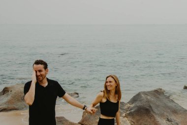 Deniz kenarındaki kayalıklarda el ele tutuşan beyaz bir çift..