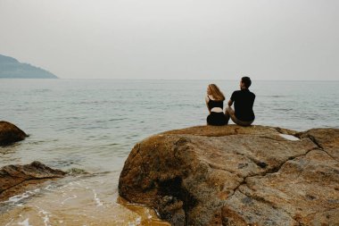 Çift bulutlu gökyüzünün altındaki kayaların üzerinde sakin sahil manzarasının keyfini çıkarıyor..