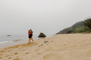 Okyanus manzaralı kumsalda kucaklaşan bir çift..