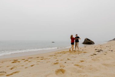 Kumsal yürüyüşünden hoşlanan çift: genç beyaz erkek ve dişi kumlu sahilde kucaklaşıyor.