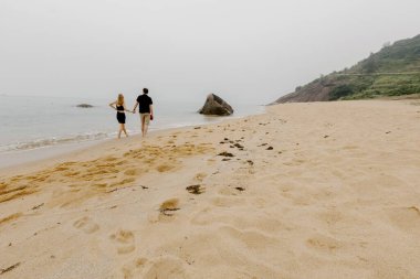 Okyanus kıyısında kumlu sahilde yürüyen bulutlu bir çift..