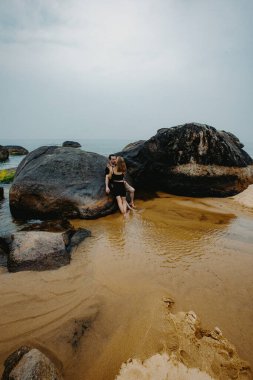 Bulutlu bir günde kayalık bir sahilde eğlenen genç beyaz bir çift..