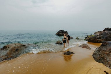 Bulutlu bir havada kayalık sahilde yürüyen beyaz bir çift..