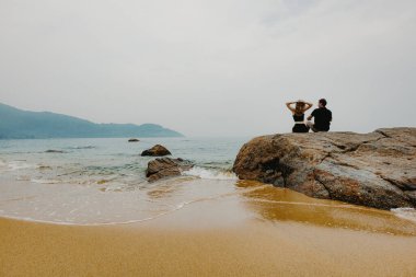 Okyanusa bakan kayalıklarda oturan beyaz yetişkinler..