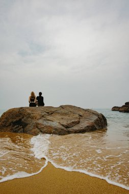 Huzurlu sahil sahnesi. İki yetişkin okyanus kıyısında kayalarda dinleniyor..