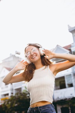 Genç beyaz kadın şehir ortamında kulaklıklarla açık havada müzik dinliyor..