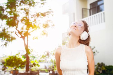 Kafkasyalı genç bir kadın açık havada, kulaklıklarla müzik dinliyor..