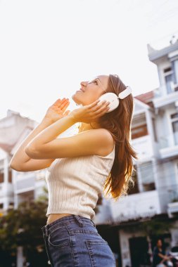 Genç beyaz kadın kulaklıklarla açık havada müzik dinliyor..