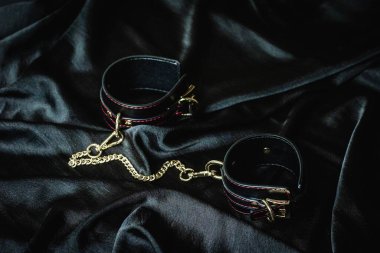 Koyu saten kumaş üzerine altın zincirli siyah deri kelepçeler..