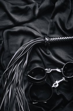 Siyah deri kelepçeler ve saten kumaş kırbaç..