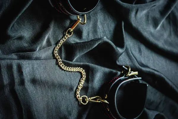Koyu renk kumaş yüzeyinde altın zincirli siyah deri kelepçeler..