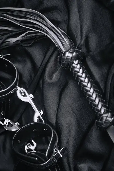 Siyah deri kamçı ve saten kumaşta kelepçe..