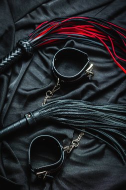 Siyah kumaşta kırbaç ve kelepçe: kırmızı ve siyah bdsm aksesuarlar.