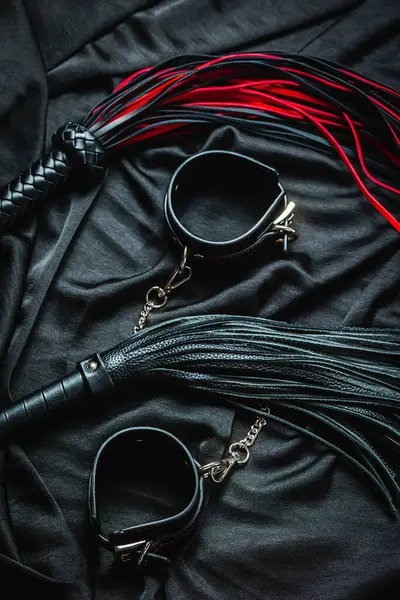 Siyah kumaşta kırbaç ve kelepçe: kırmızı ve siyah bdsm aksesuarlar.