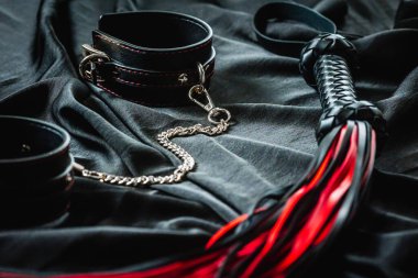 Siyah deri kemer ve kırmızı uçlu kırbaç. Koyu renk kumaş arka planda..